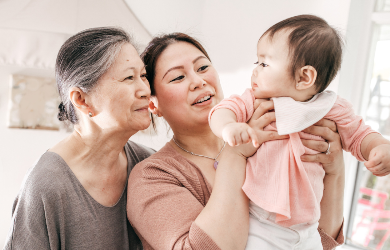 Three generations—an older woman, a younger mother, and a baby—share a warm moment together, symbolizing support through every stage of life.