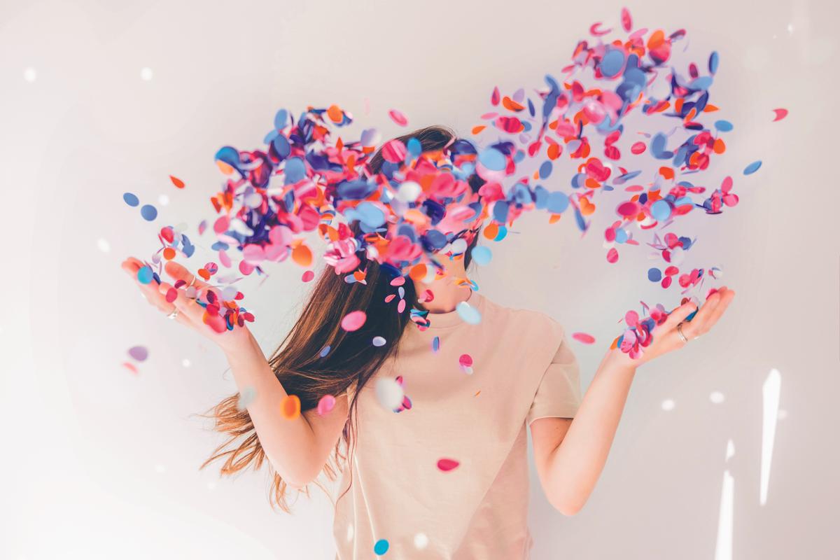 Woman celebrating with confetti on white background.