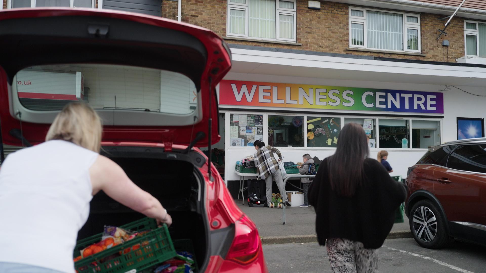 Two people taking food donations out of a car boot and into a community centre for a food bank