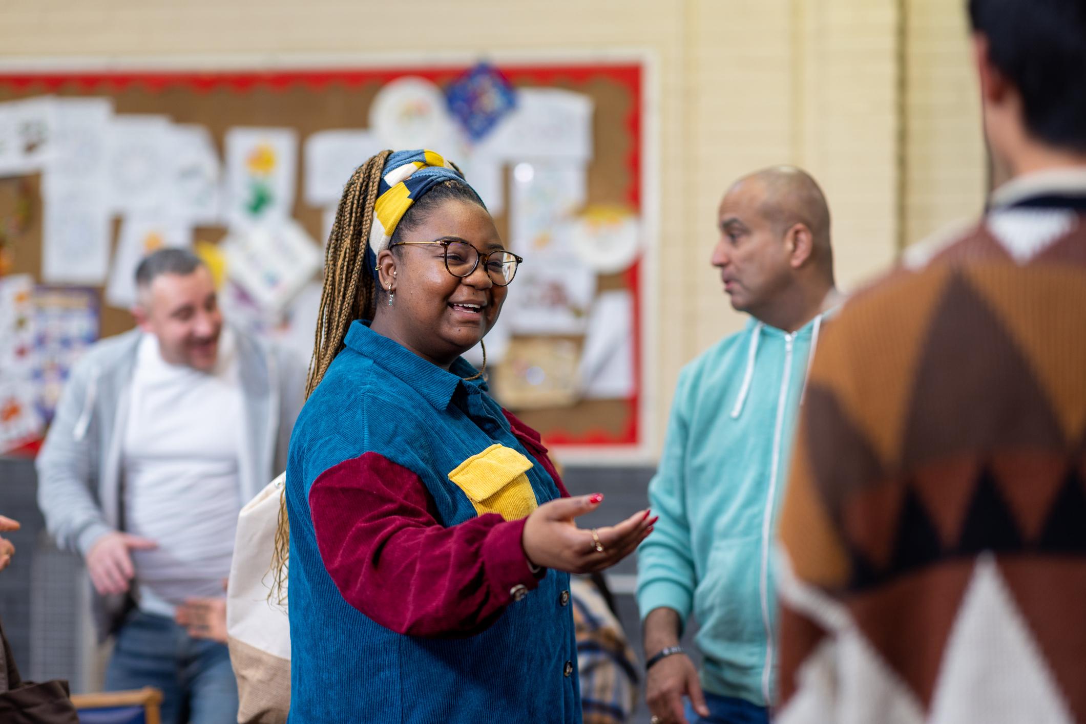 Over the shoulder shot of a group of adults greeting each other, ready to talk to each other about their mental well-being. They are all wearing casual clothing. The community centre is located in Seaton Deleval in the North East of England.