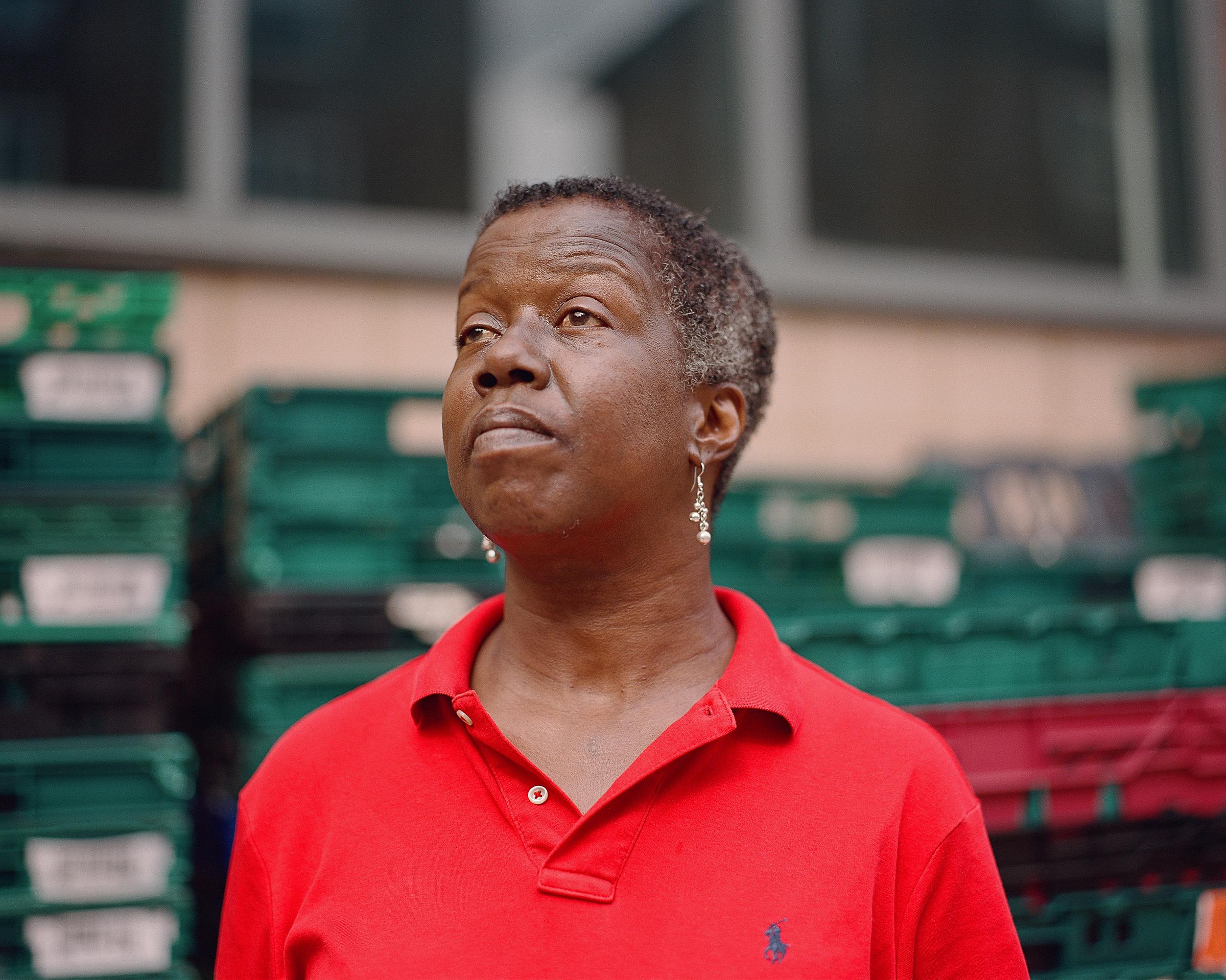 Food bank volunteer wearing a red polo shirt stood in front of food crates looking into the distance.