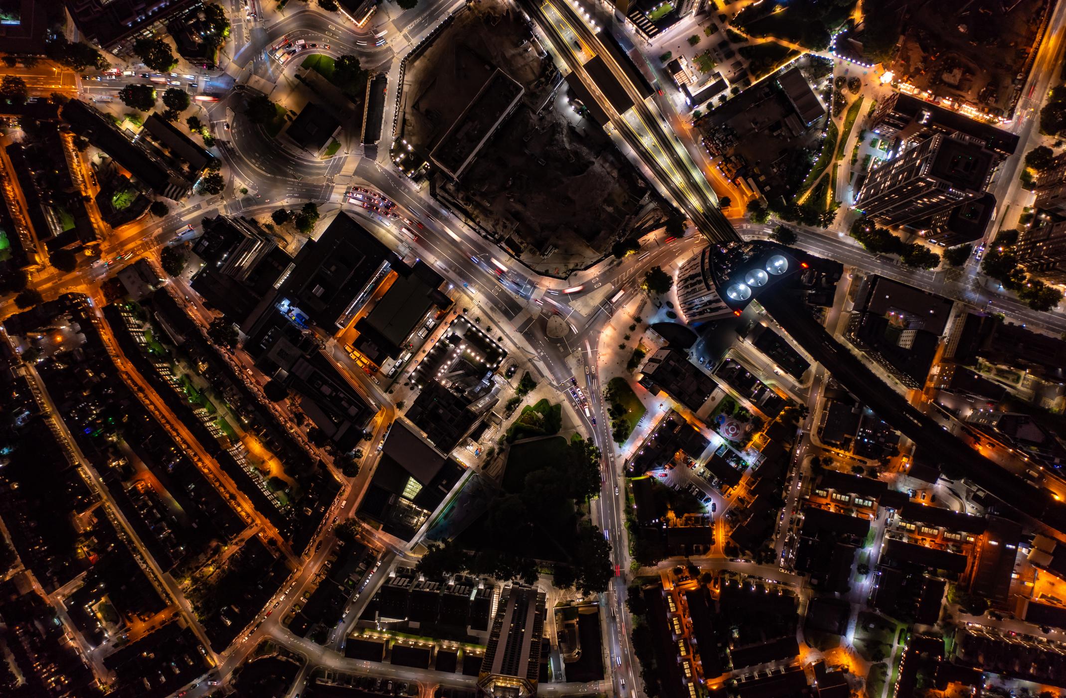 Birds eye view of tall financial and commercial buildings with shadow and cars moving on city street during night with illuminated lights in London city.