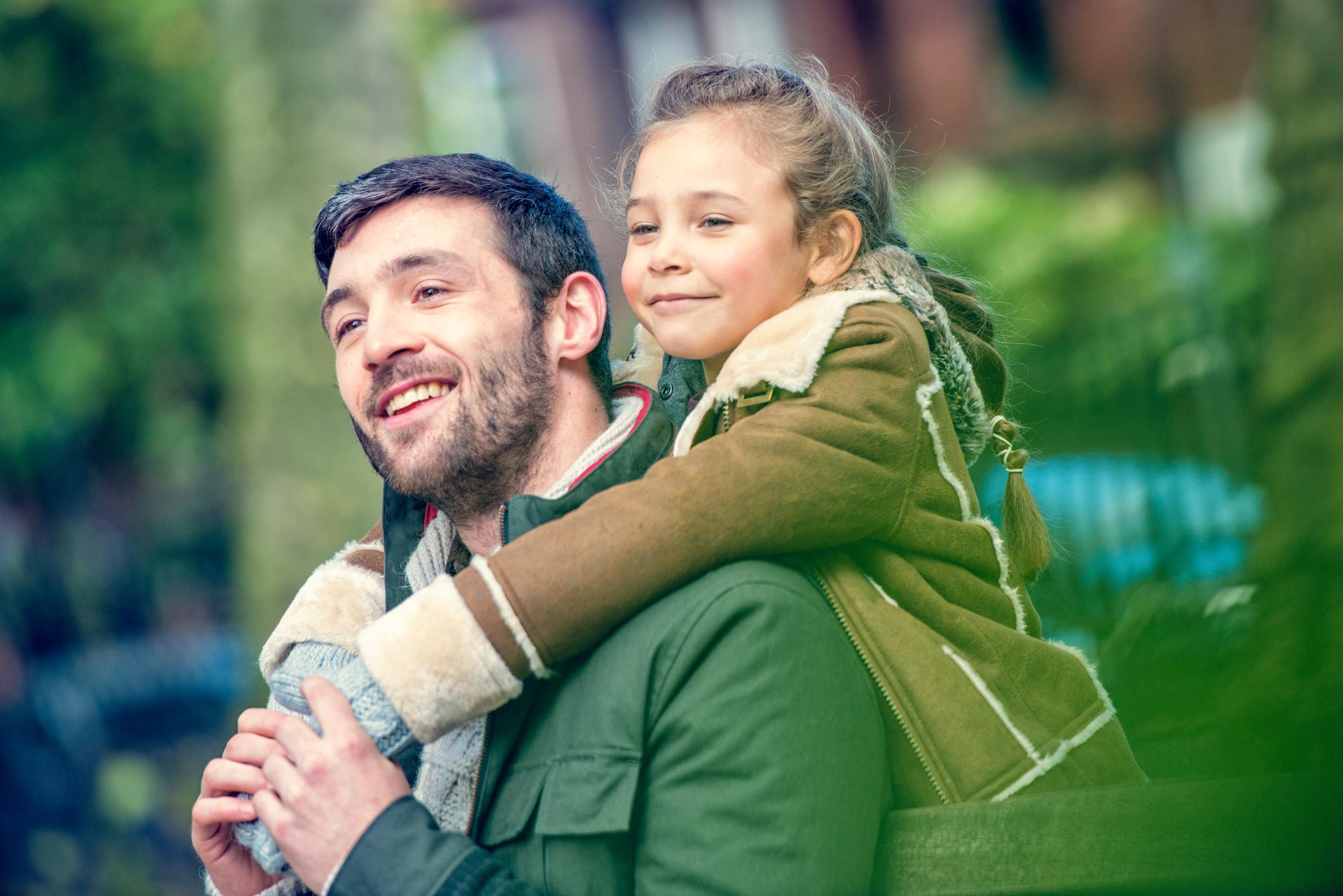 Father and daughter in a park, smiling.