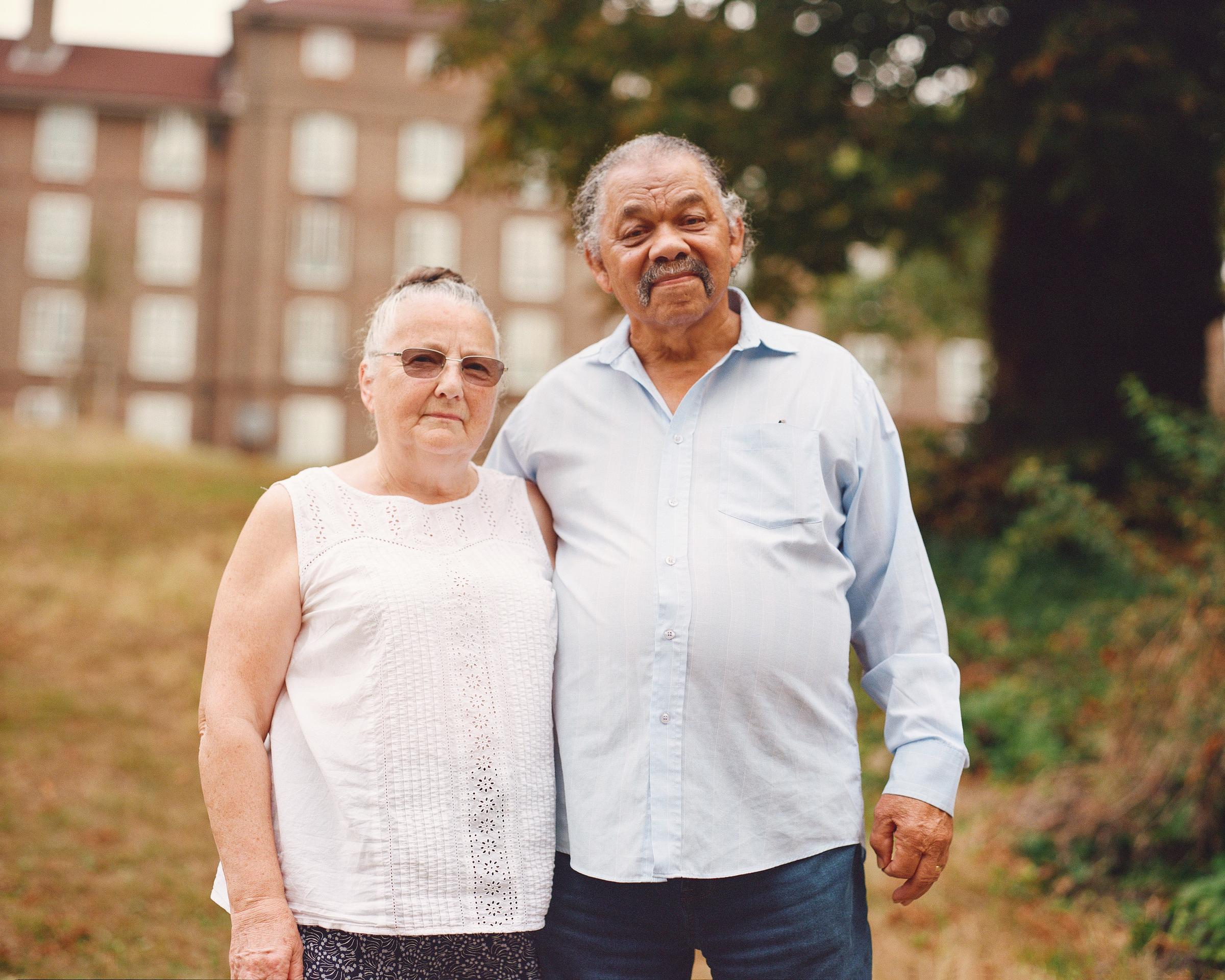 A man and a woman standing in front of a building and trees.