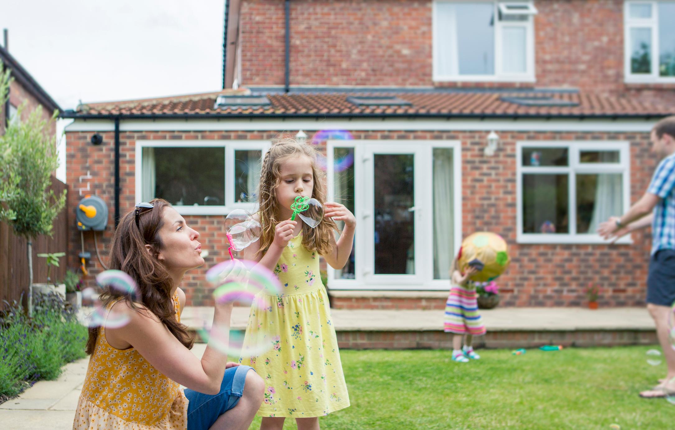 Mother and daughter playing together in the garden blowing bubbles.