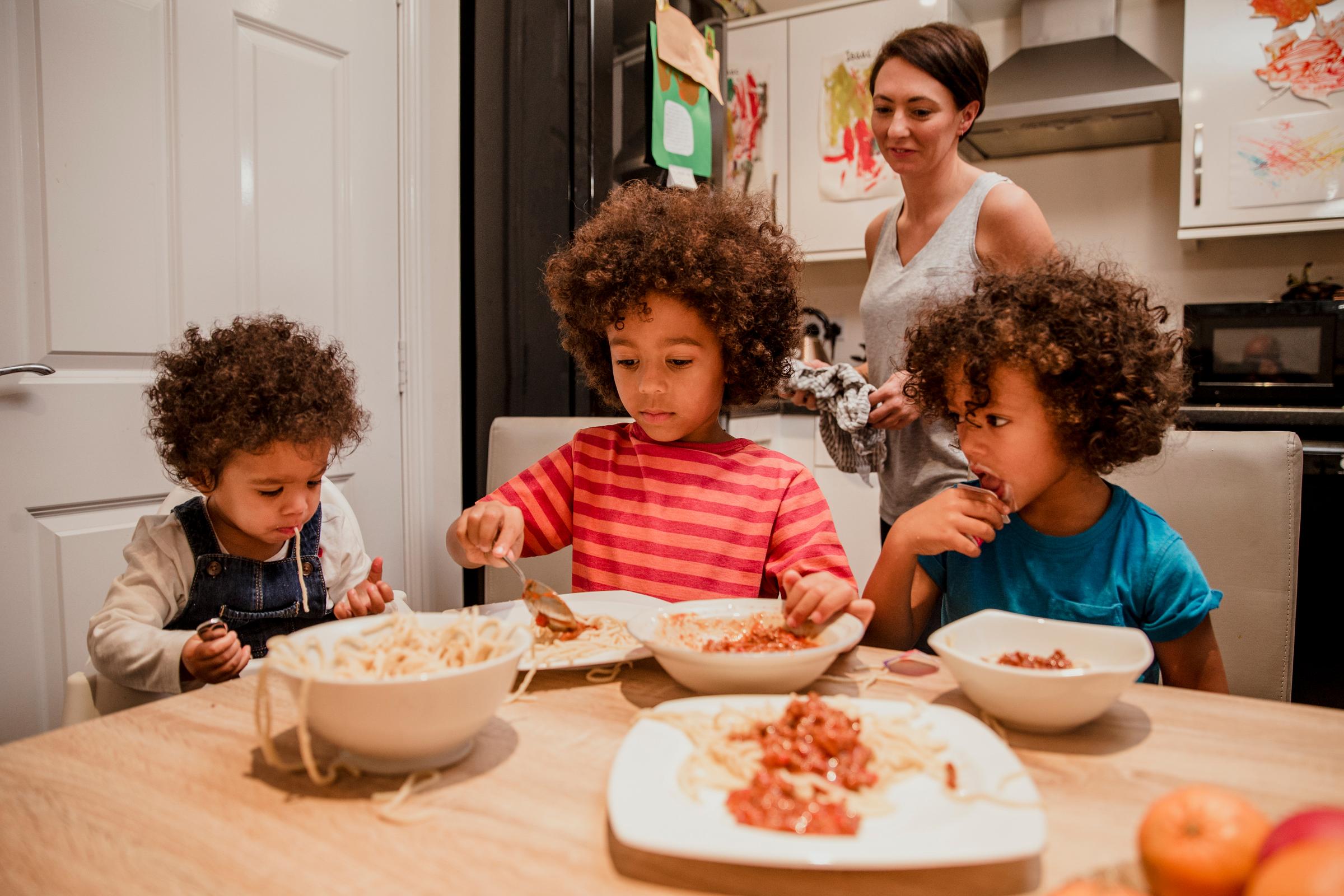 A family around a table eating spaghetti mum is watching from behind
