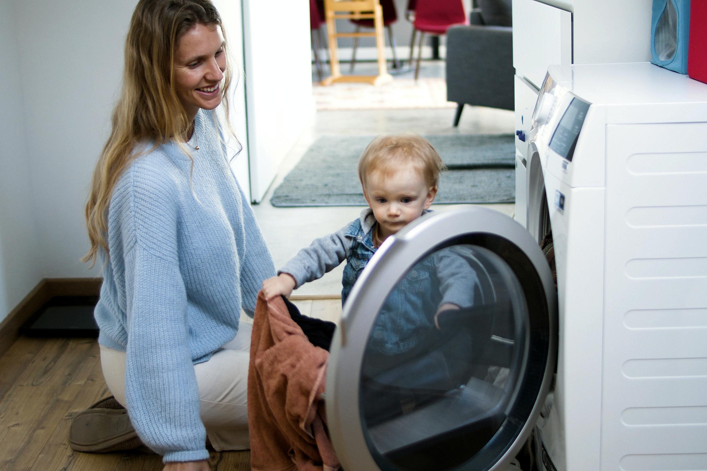 Woman and toddler knelt on floor putting laundry into washing machine