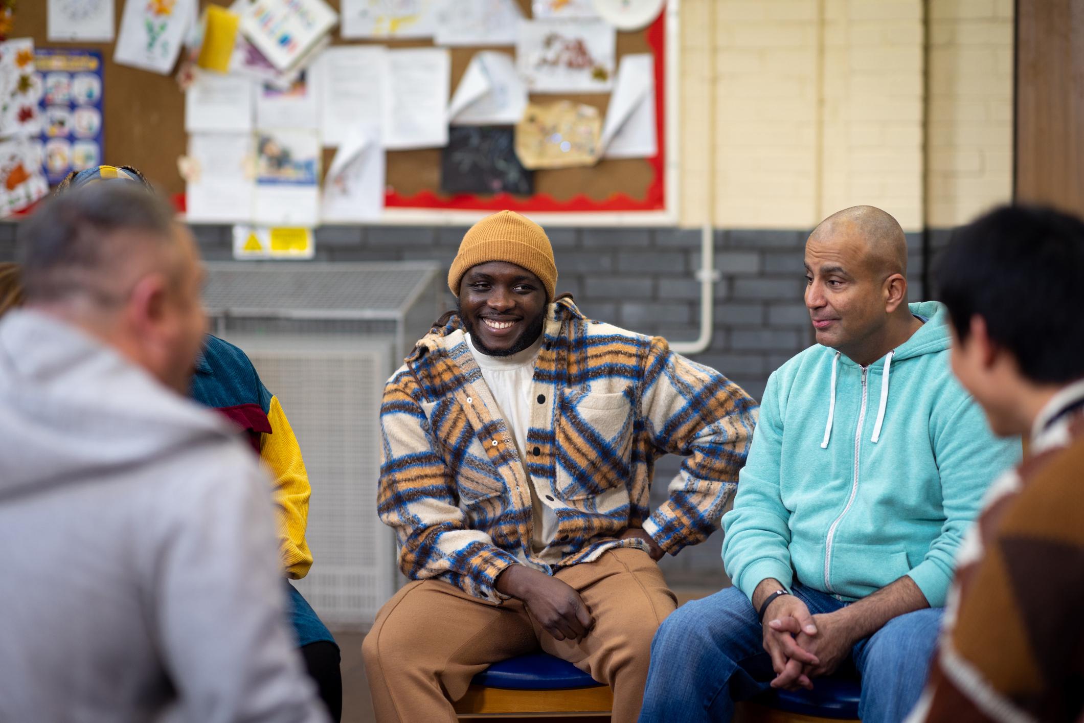 Men smiling in round circle at community centre