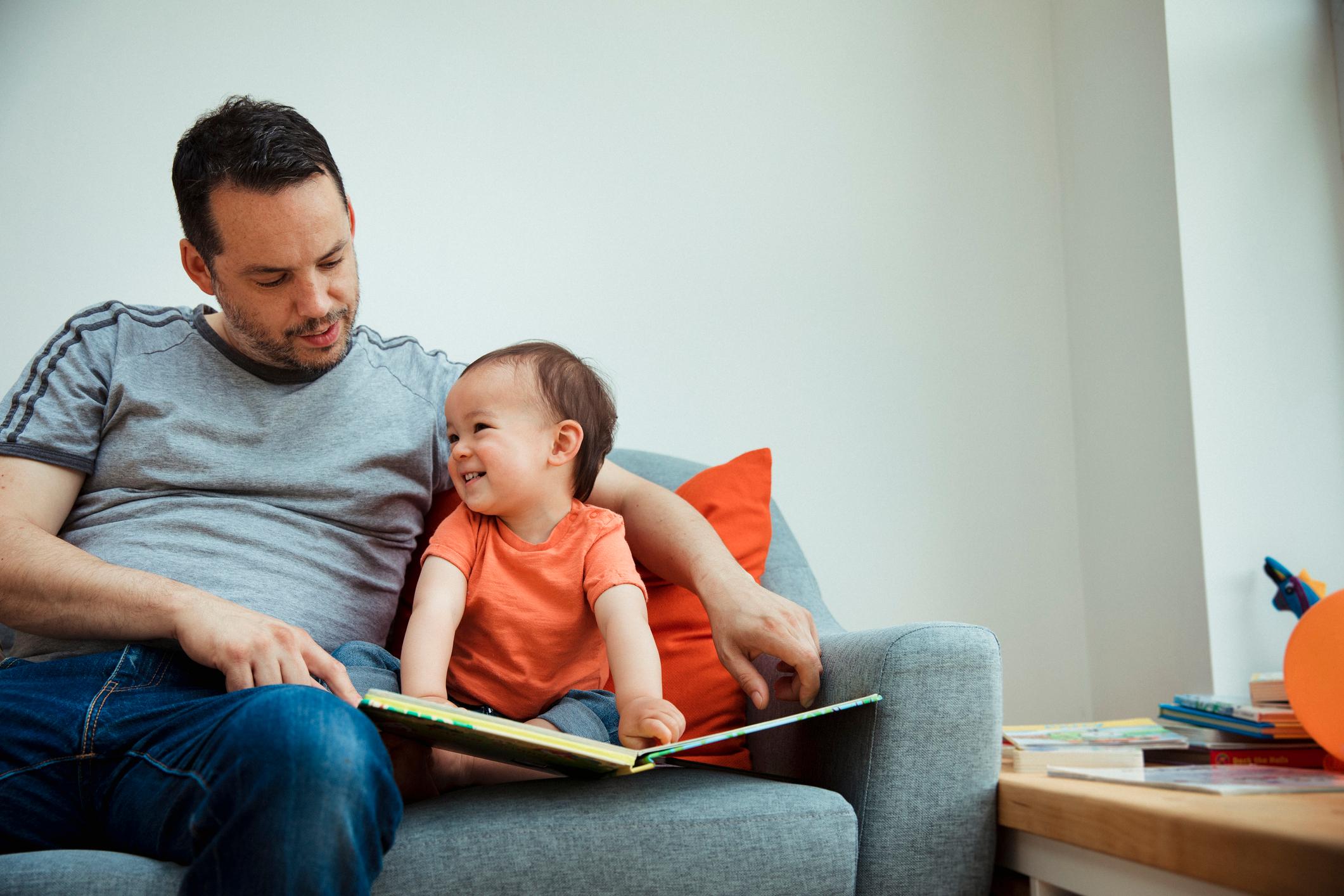 Father and child sat together reading and smiling.
