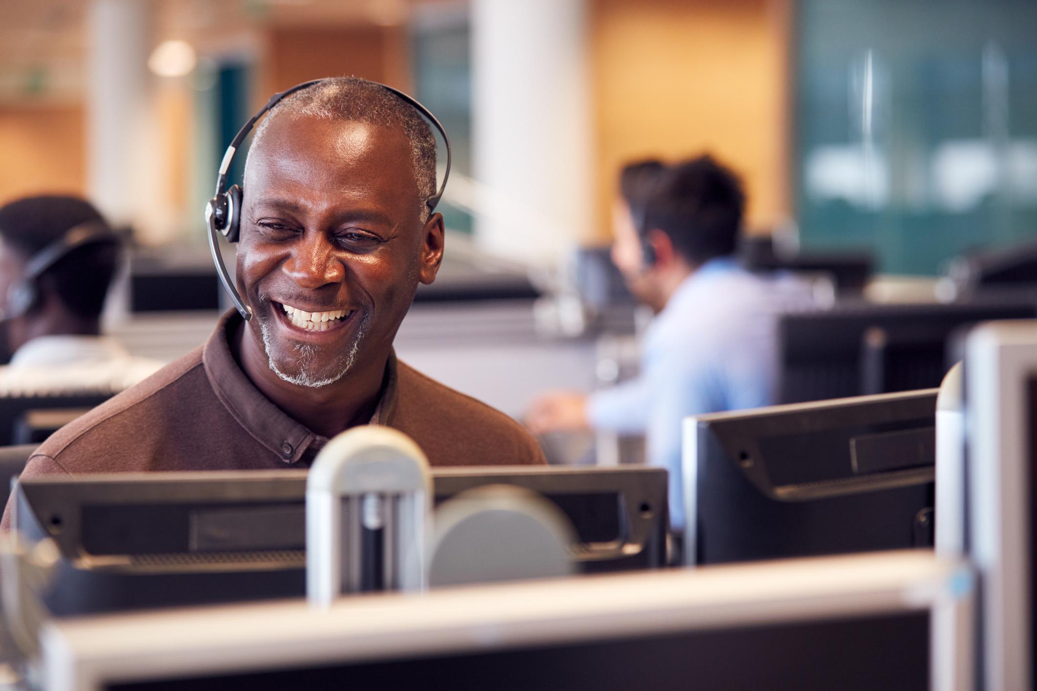 Businessman wearing telephone headset whilst talking and smiling.