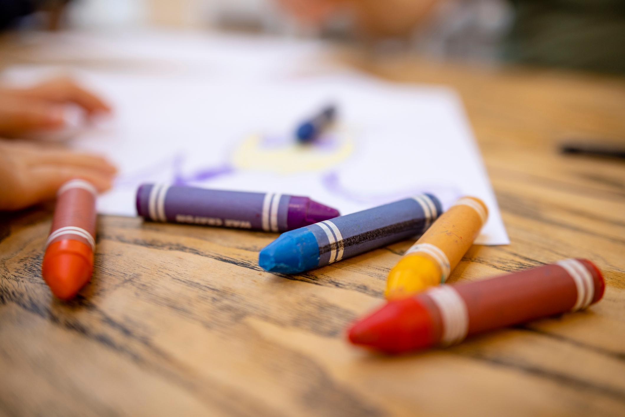 A close-up shot of colourful crayons on a wooden table with paper.