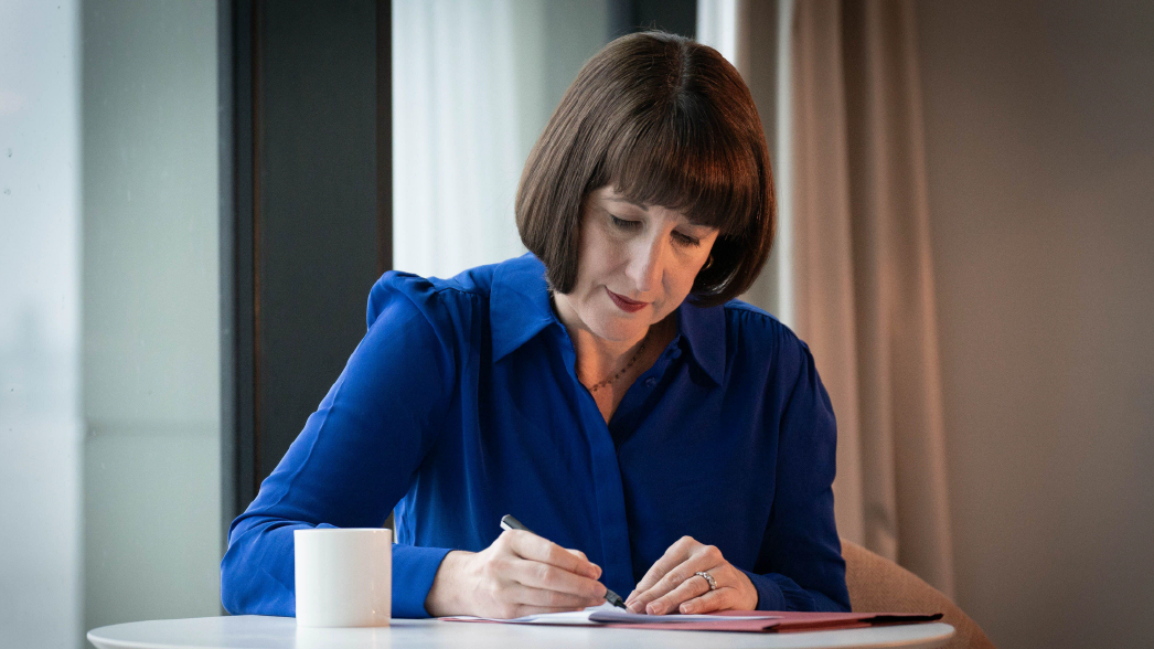 Chancellor of the Exchequer - Rachel Reeves - sat at a table writing with a pen on paper.