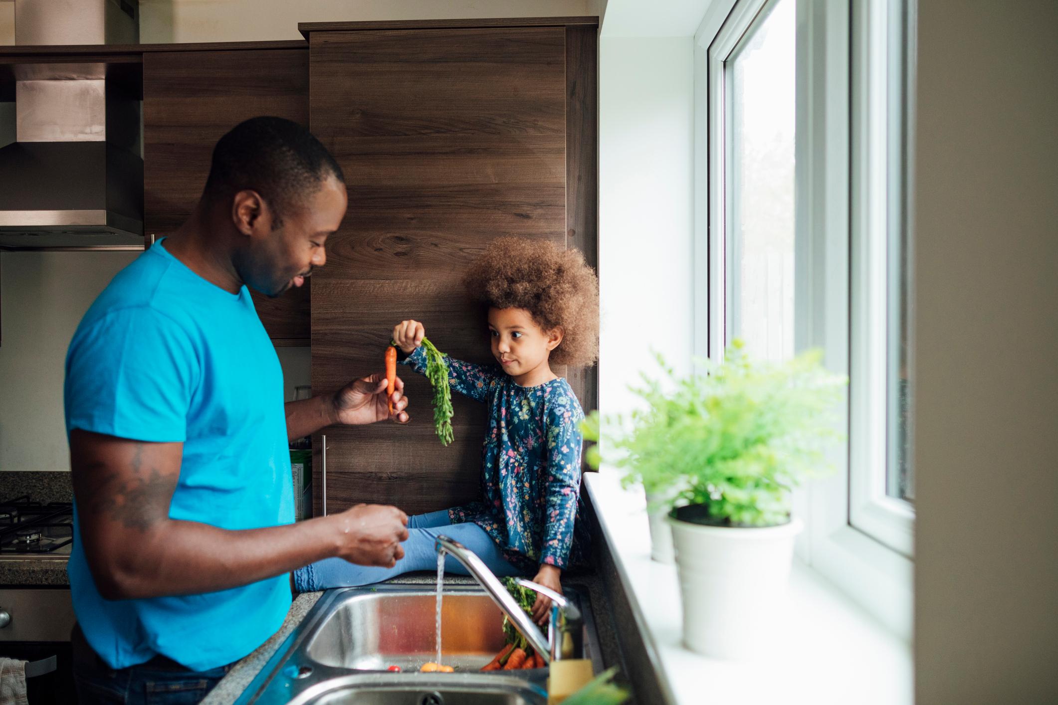 Father and daghter washing vegetables in the sink at home.