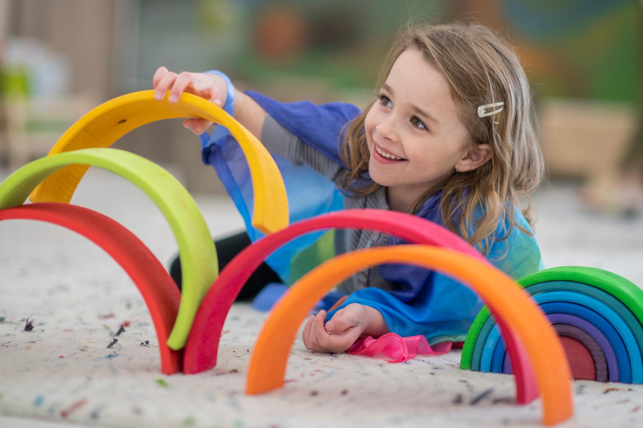 A girl places colourful rings on top of each other while smiling. 