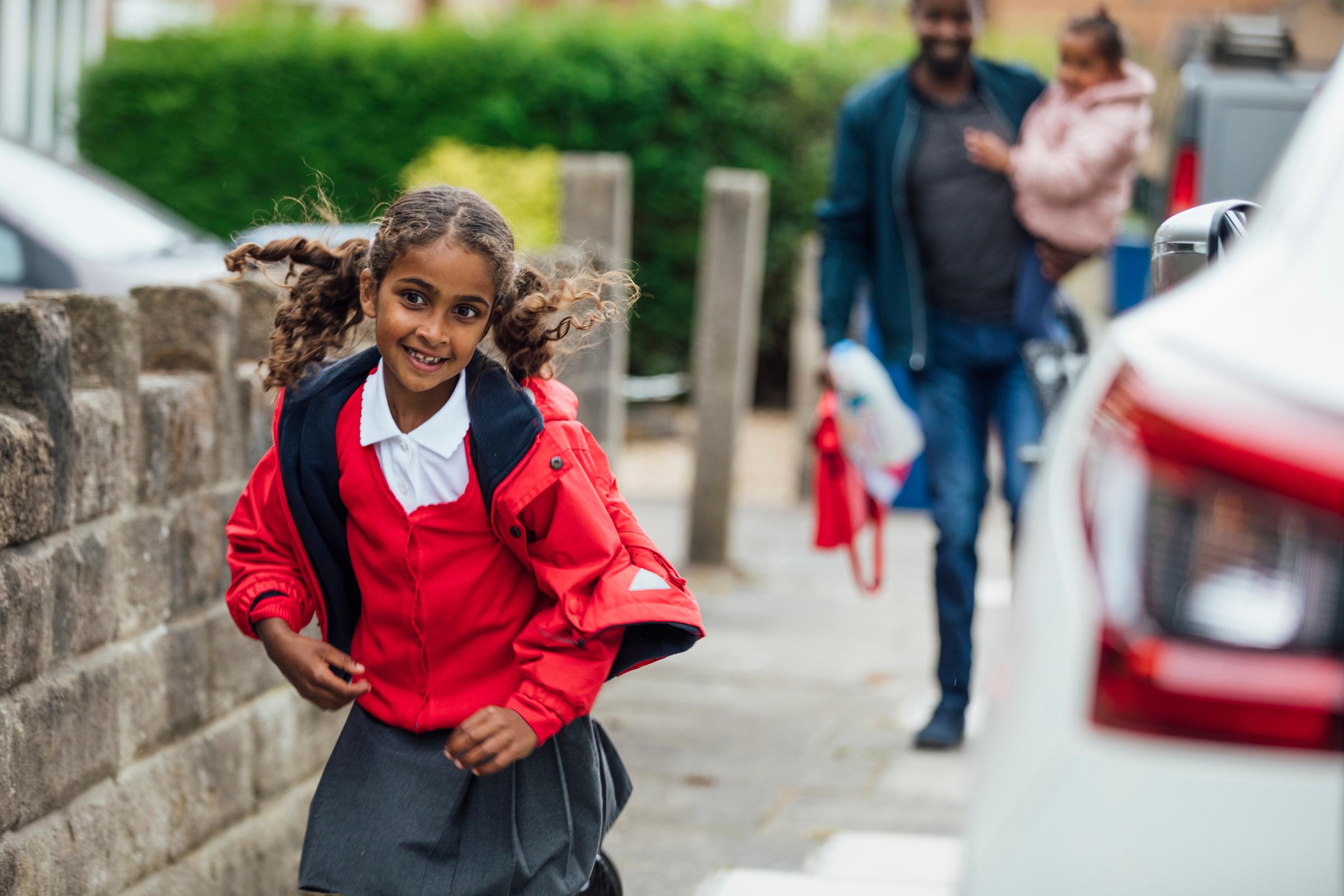 Young girl running as she leaves school with her father and her sister.
