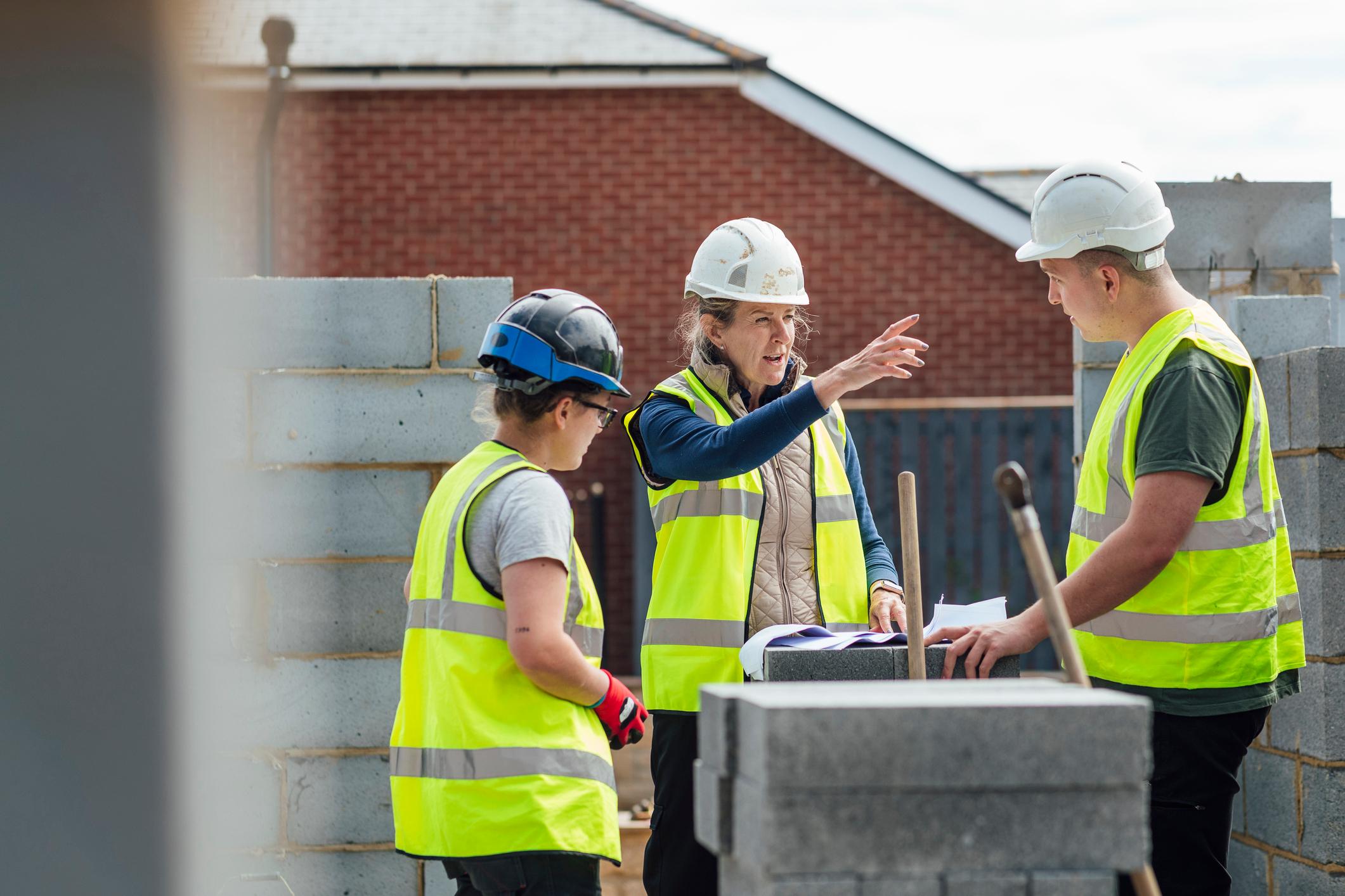 A site manager and two construction workers meeting on-site having a conversation.