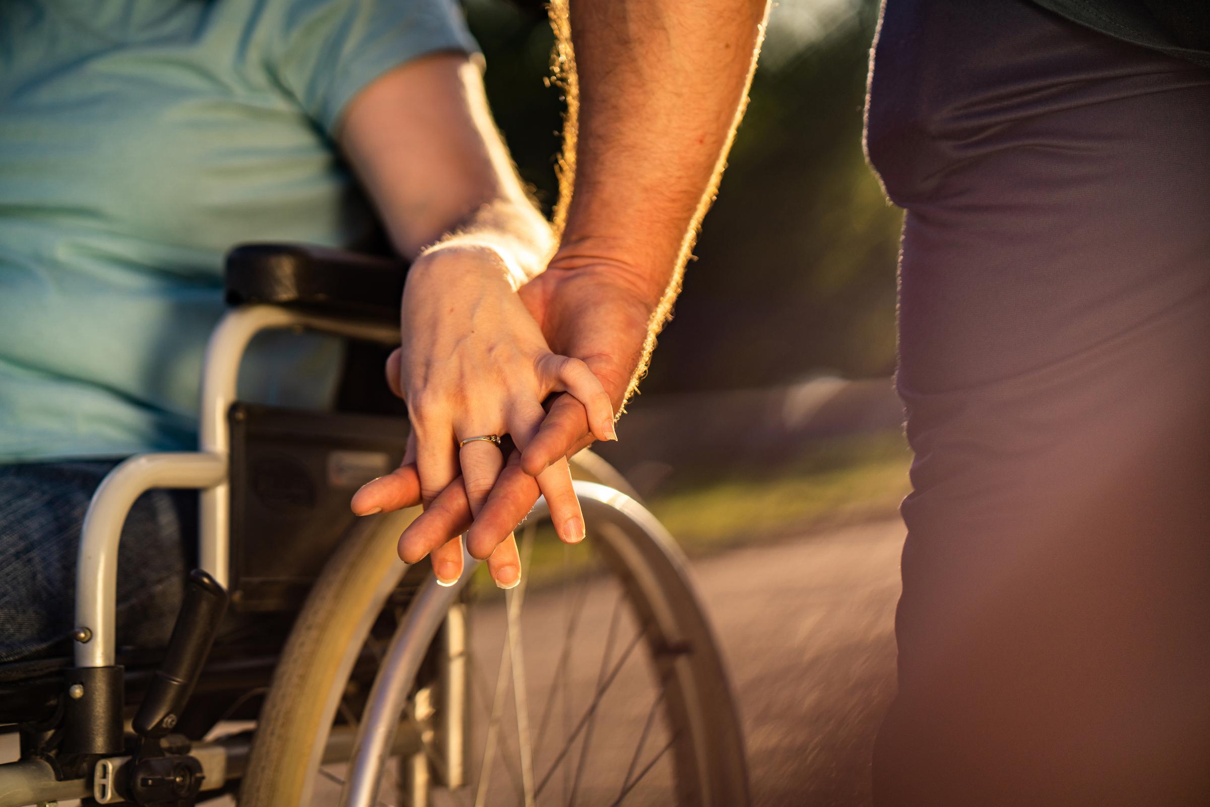 Close up hands of walking couple, women in wheelchair