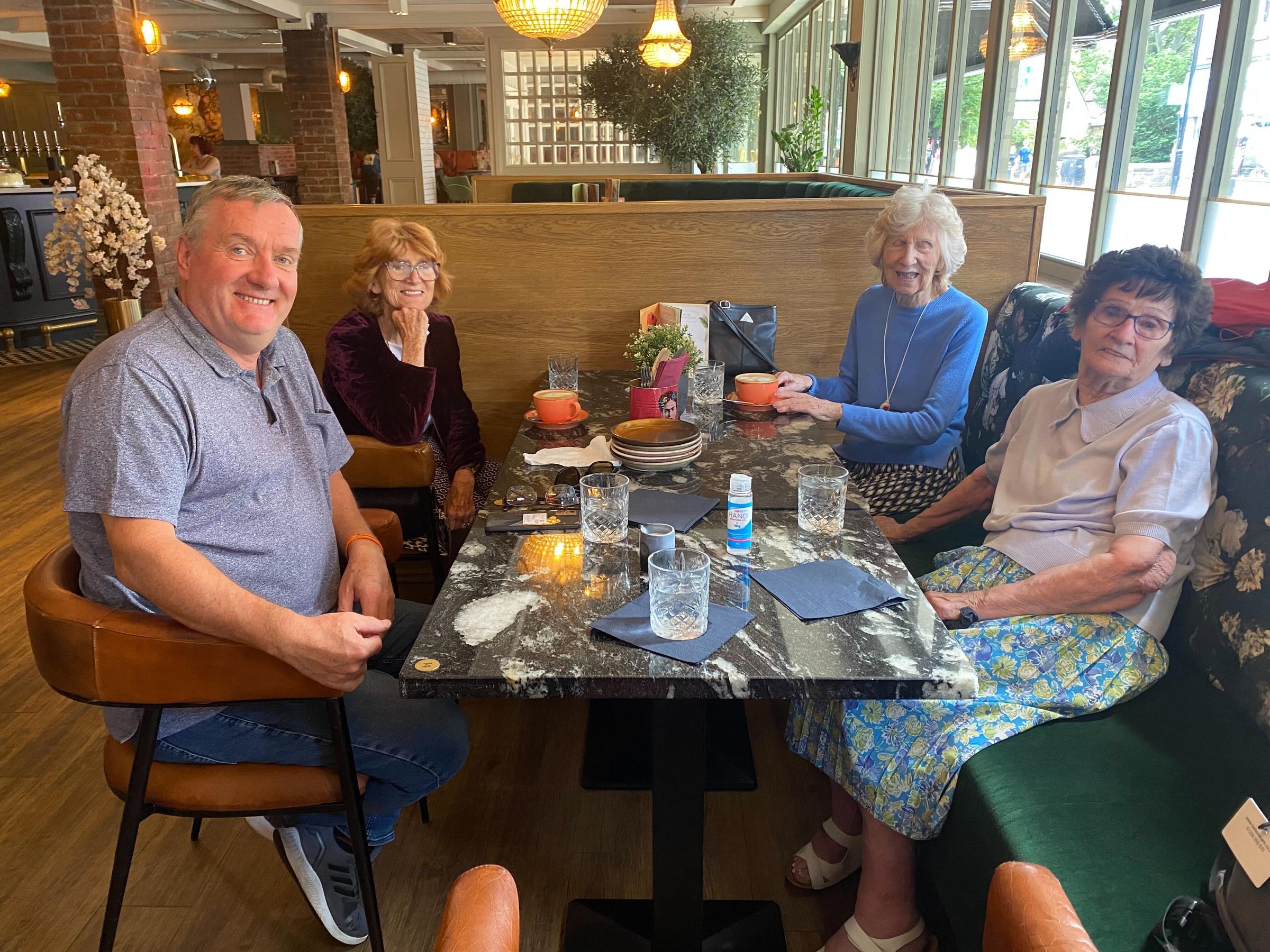 Residents of a care home sat round a table drinking coffee and smiling for photo