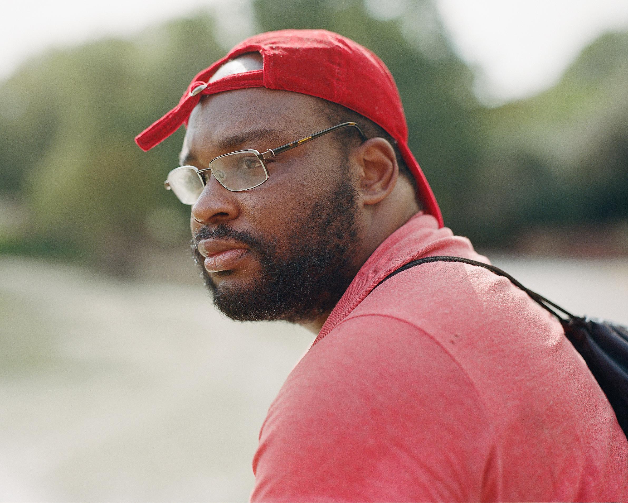 Young man sat on a bench, looking into the distance with a cap on.