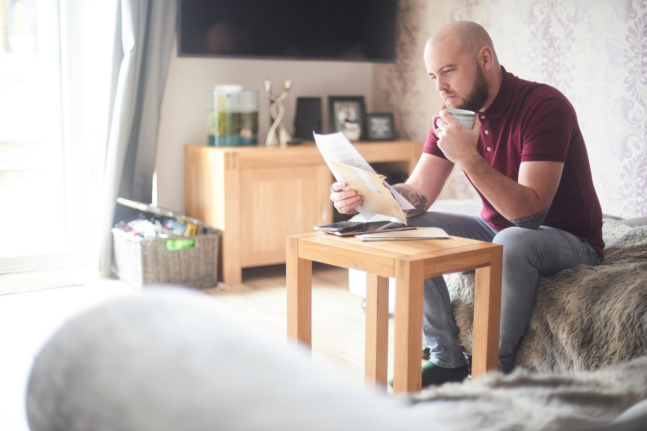 Homeowner reading paperwork sat on the sofa in his living room.