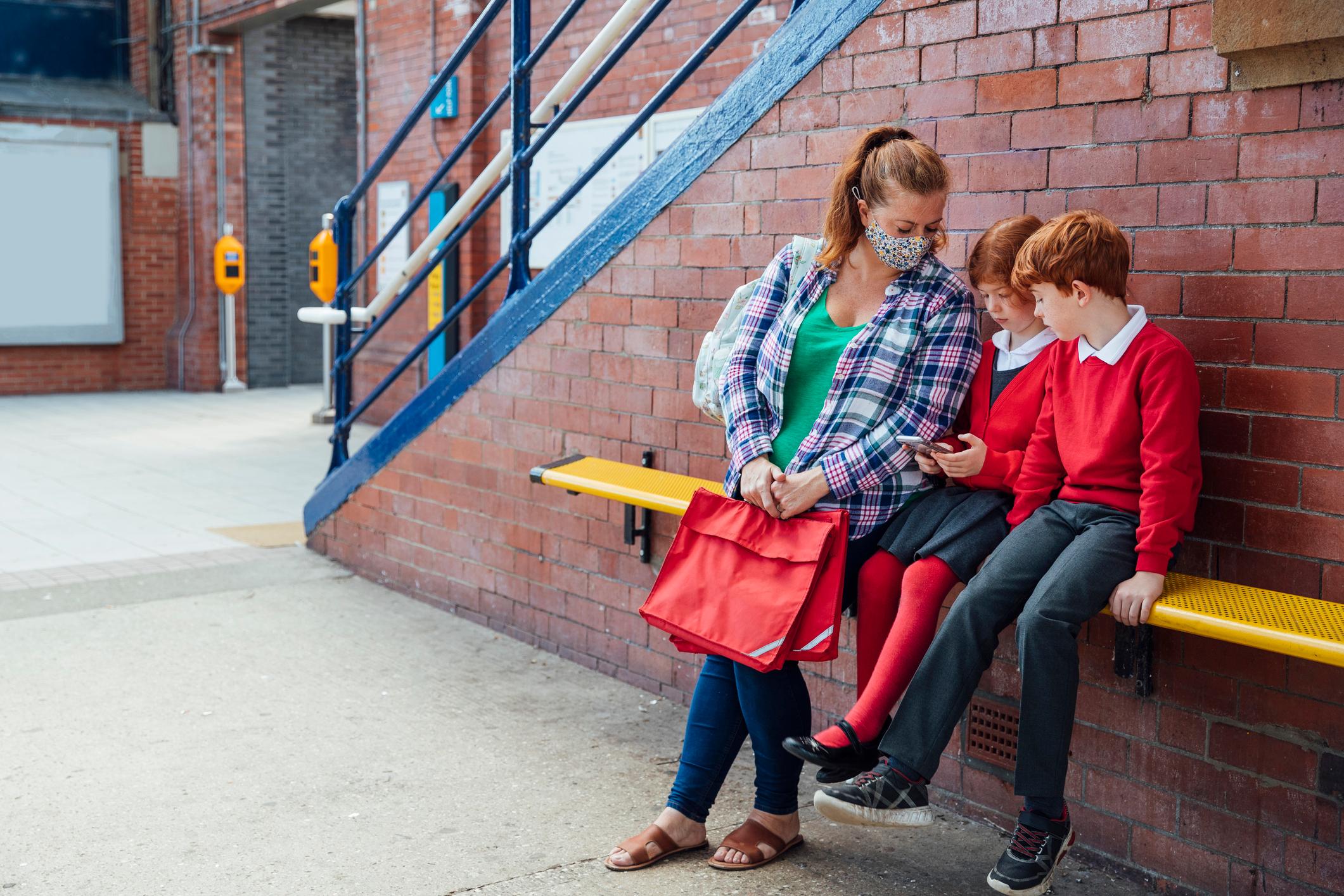 A mother sits with her children the train station waiting for the train to take them to school.