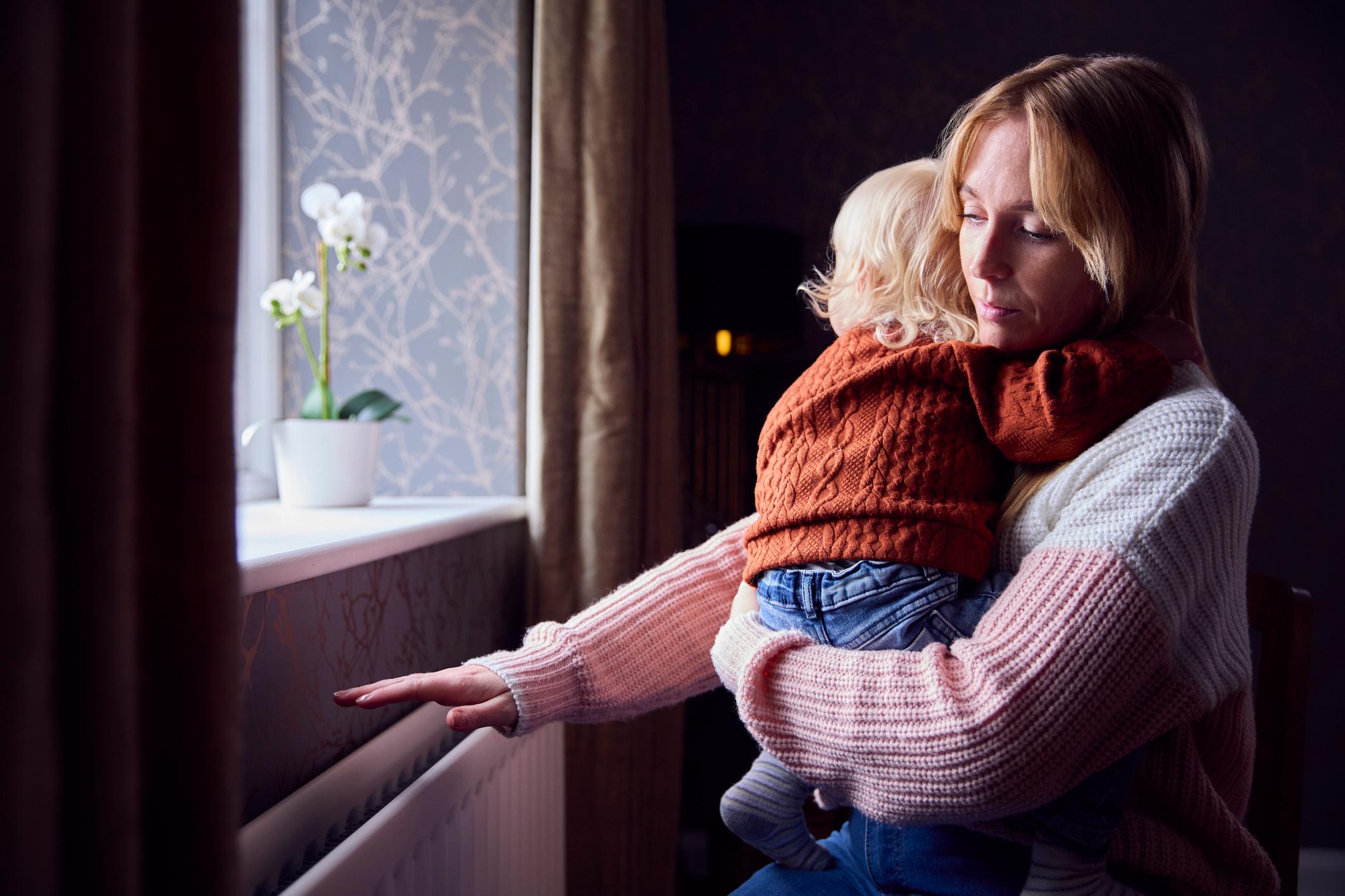 Mother and son trying to keep warm by a radiator at home.