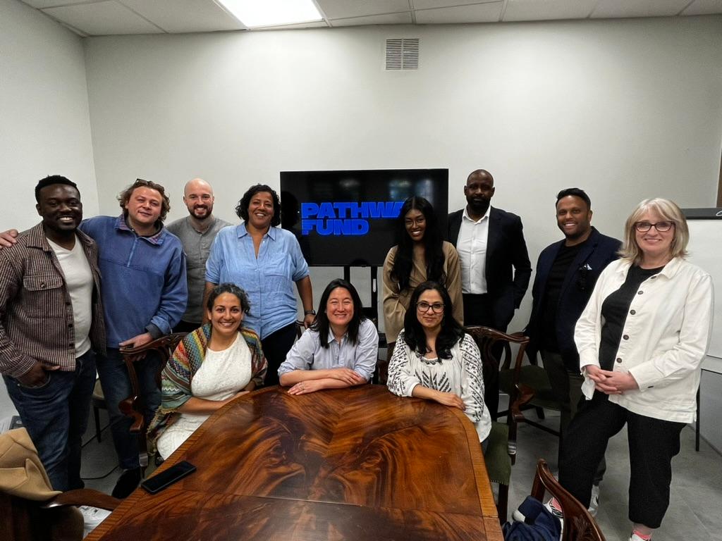 Team of people sat and stood around board table smiling for photo