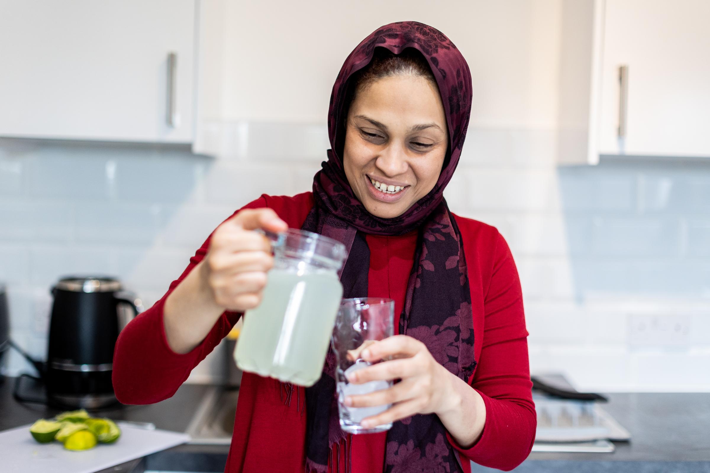 Woman pouring a drink and smiling in a kitchen.