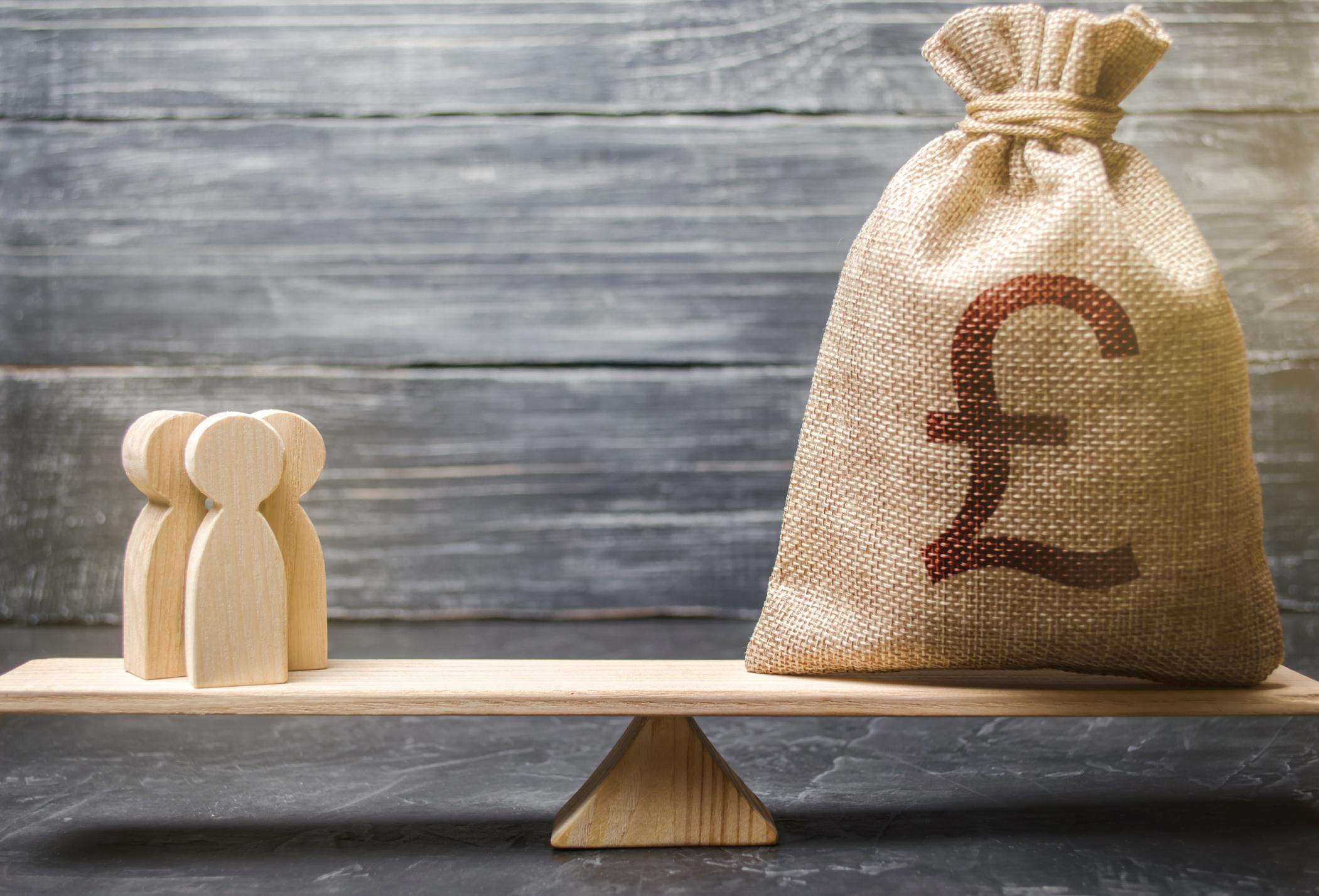 A set of wooden scales balancing three wooden people and a money bag equally.