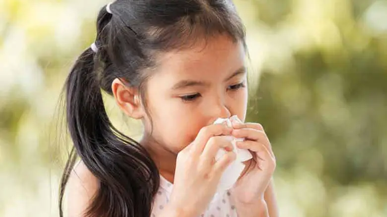 A child blowing her nose into a tissue.