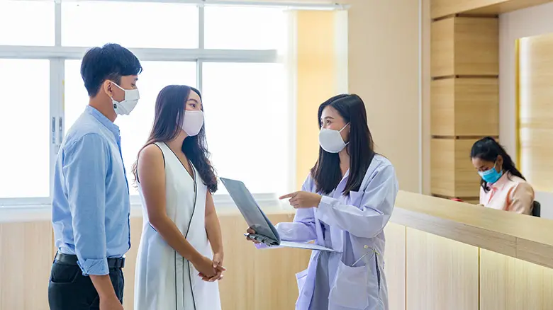 The doctor is talking to a couple to plan a family in the hospital. The doctor is talking to a couple to plan a family in the hospital. Couple - Relationship Stock Photo