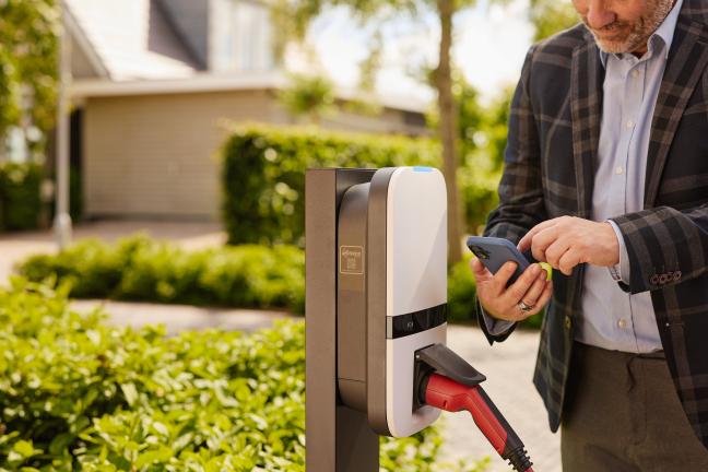 man op de mobiel bij een donkergrijze laadpaal met aangesloten auto