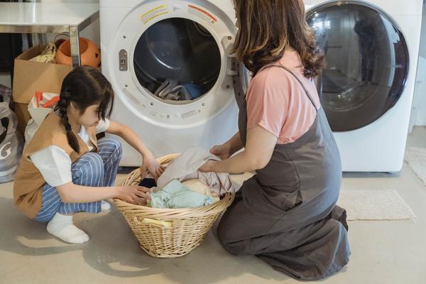 Een moeder en dochter zitten samen bij een wasmachine naast een mand met schone was