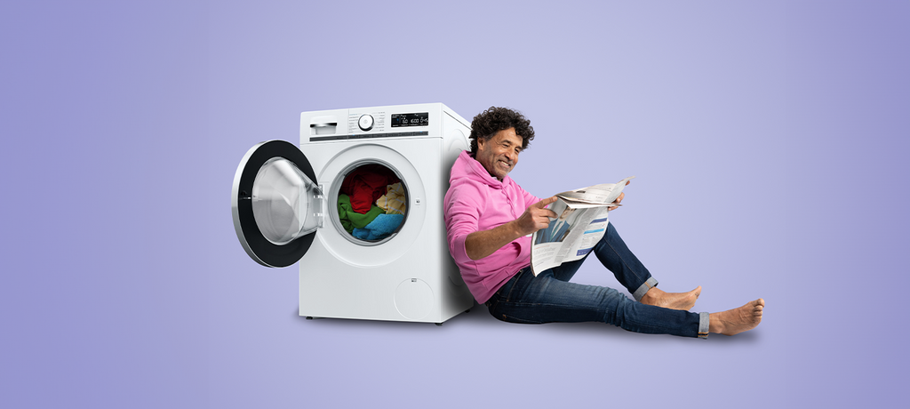 Man leest krant leunend tegen de wasmachine
