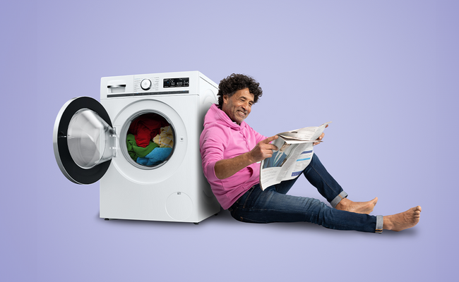 Man leest krant leunend tegen de wasmachine