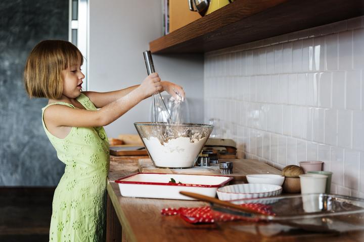 Meisje staat in de keuken en roert in een kom