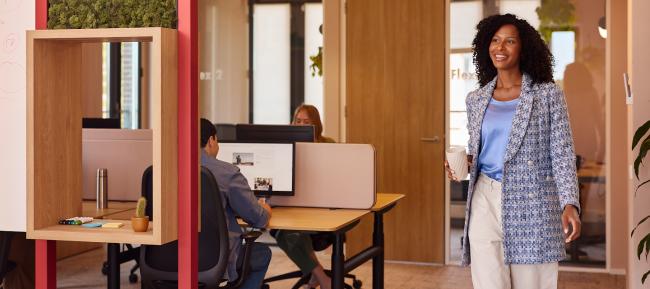 Een lachende zakenvrouw loopt door kantoor met een mok in haar handen