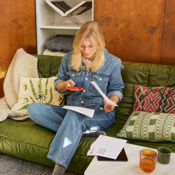 Femme avec des factures et un smartphone sur un canapé