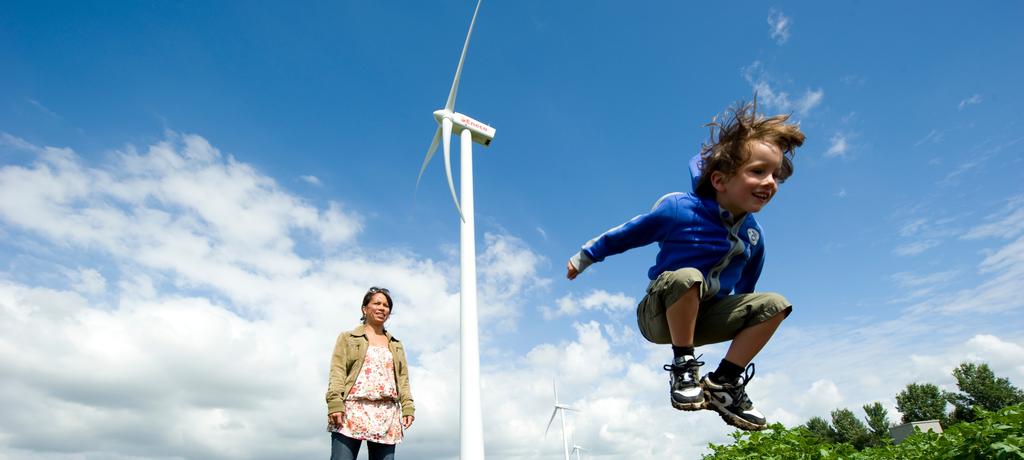 Een moeder met kind bij een windpark, de jongen springt in de lucht. 