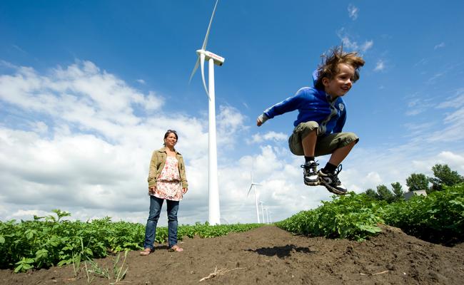 Een moeder met kind bij een windpark, de jongen springt in de lucht. 