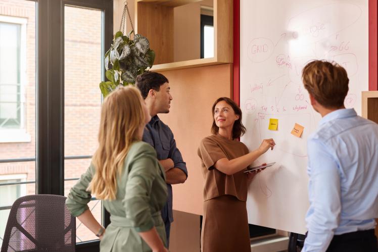 Des employés de bureau discutent devant un tableau blanc.