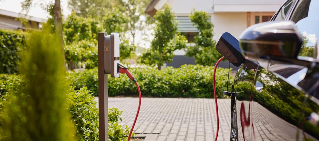 zwarte elektrische auto met rode kabel aan wit met grijze laadpaal gekoppeld 