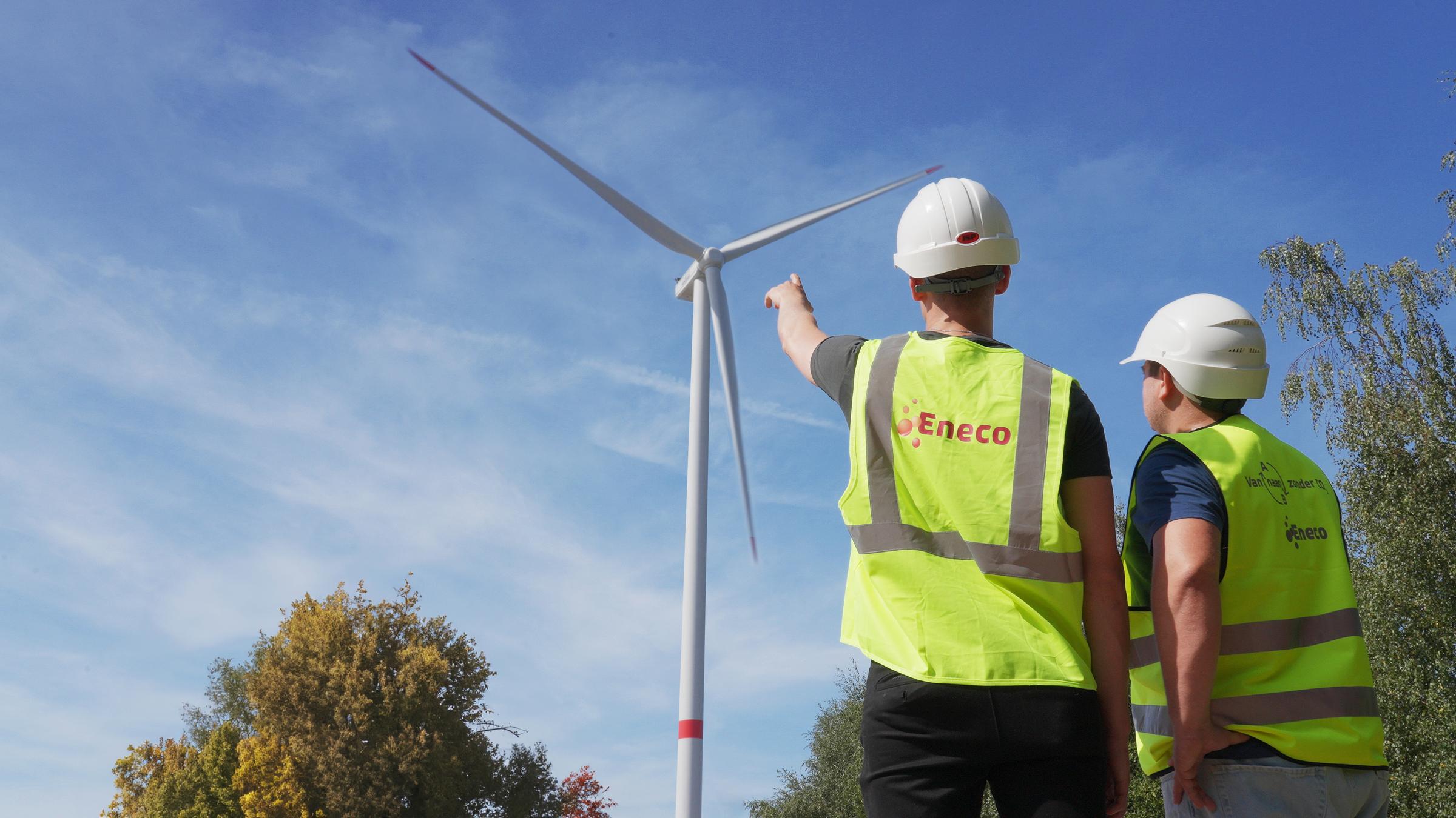 Een Eneco-technieker wijst een windmolen in de verte aan voor zijn collega