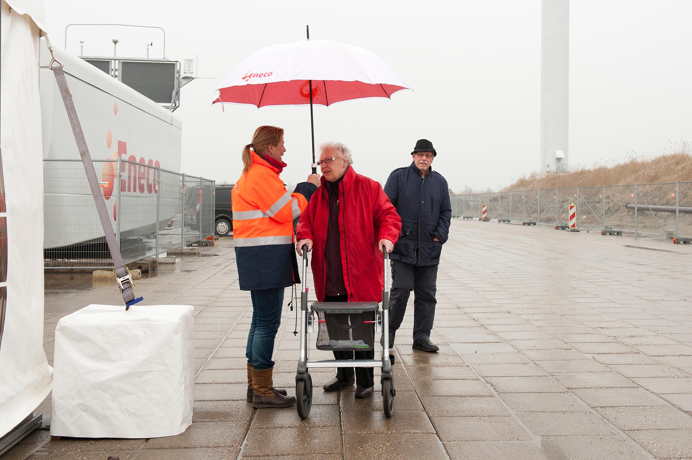 Regen in de windpark Delfzijl Noord, vrouw biedt haar paraplu aan aan ouderen