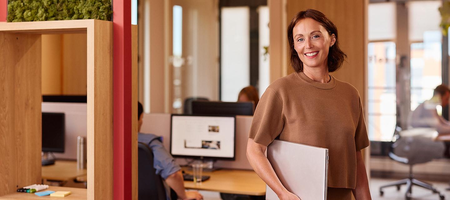 Een vrouw op kantoor met een laptop onder de arm