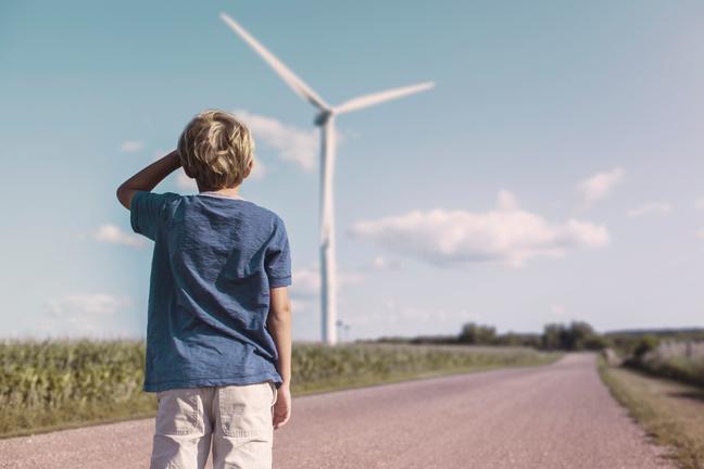 Een jongen kijkt in de verte naar een windturbine
