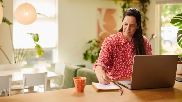 Vrouw kijkt naar de laptop en maakt aantekeningen