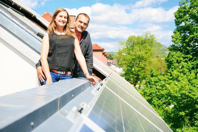 Vrouw en man staan op het balkon van hun huis naast de zonnepanelen op het dak