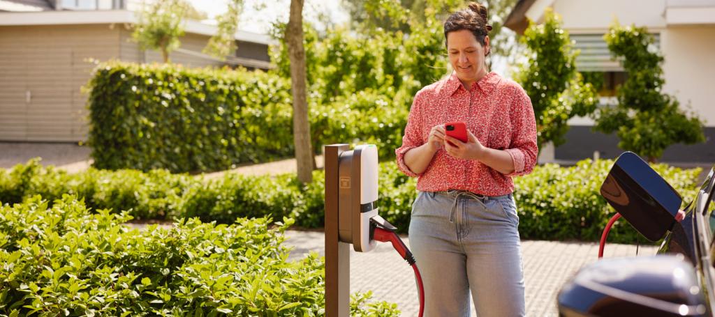 vrouw laadt haar elektrische auto op en gebruikt haar telefoon