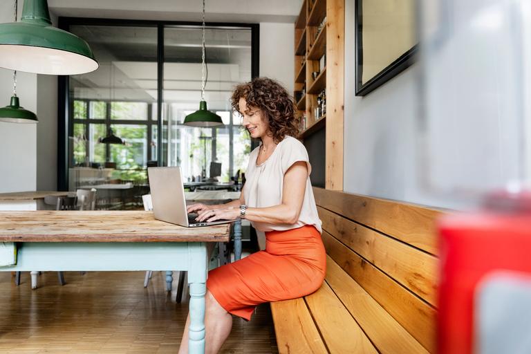 Een vrouw zit aan tafel en werkt op haar laptop